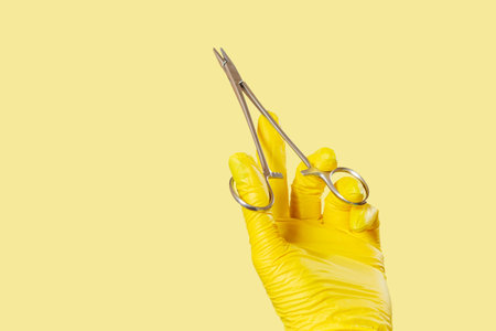 Woman's hand in a latex glove with stainless steel needle holder on yellow.の写真素材