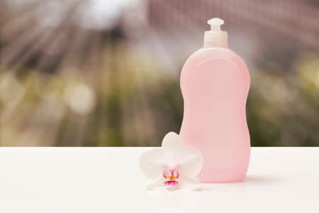 Bottle of dishwashing liquid and an orchid flower on the blurred background with sun rays. Washing and cleaning concept.の写真素材