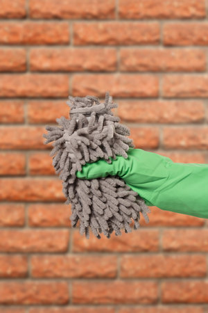 Close-up view of woman's hand in a rubber protective glove with the rag and the kitchen on the...