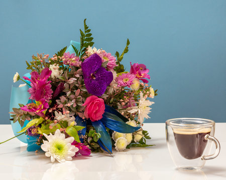 Beautiful bouquet of different flowers with a cup of coffee on the blue background.
