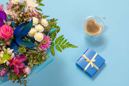 Cup of coffee, a gift box and flowers on the blue background. Top view.の写真素材