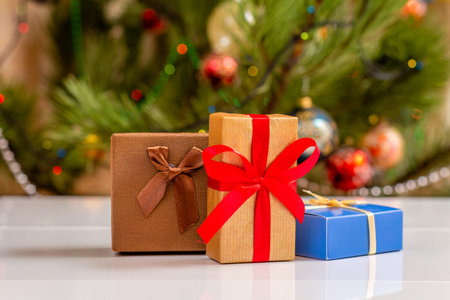 Gift boxes with bows. Christmas tree with blurred twinkling party lights and toy balls on the...