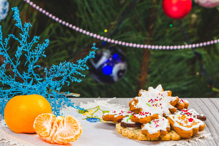 Tangerines, gingerbread cookies and a fir tree with Christmas ornaments on the background.