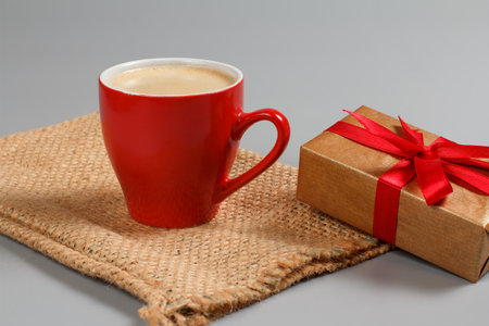 Red cup of black coffee and a gift box tied with red ribbon on the sackcloth bag. Greeting card concept.の写真素材