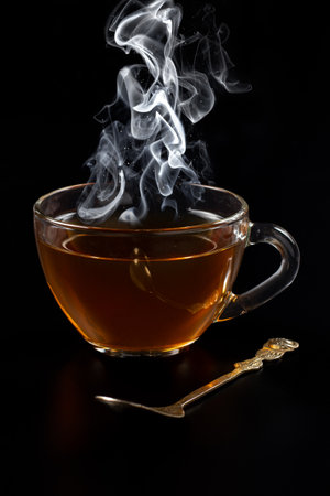 Glass cup of black tea with rising steam on the black background.の写真素材