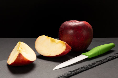 Whole apple with sliced one and a knife on the black stone cutting board. Organic fruits.の写真素材
