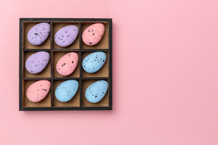 Colorful Easter eggs in a wooden box on the pink background with a copy space. Top view.