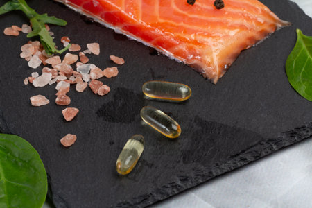 Fillet of raw salmon fish, arugula, basil leaves, salt and capsules with fish oil on the cutting board. Top view.の写真素材