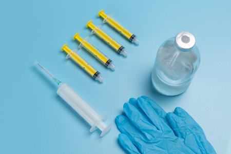 Blue latex gloves, a glass bottle for liquid medicine and syringes for injection on the blue background. Top view. Health and medical concept.の写真素材