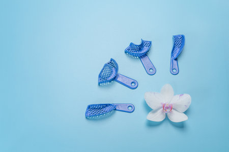 Set of dental flexible impression trays with an orchid flower on the blue background. Top view.の写真素材