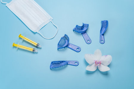 Set of dental flexible impression trays with plastic syringes and a medical mask on the blue background. Top view.の写真素材