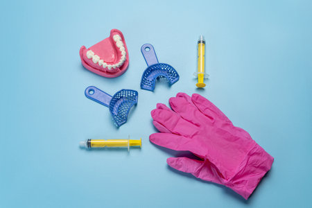 Dental flexible impression trays with a layout of the human jaw, latex gloves and plastic syringes on the blue background. Top view.の写真素材