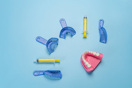 Set of dental flexible impression trays with a layout of the human jaw and plastic syringes on the blue background. Top view.の写真素材