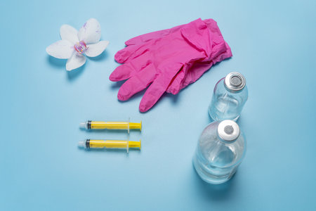 Pink latex gloves, glass bottles of liquid medicine and syringes for injection on the blue background. Top view. Health and medical concept.の写真素材