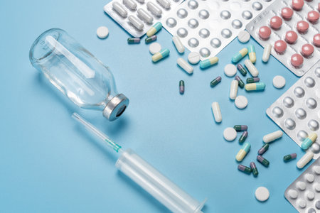 Glass bottle of liquid medicine, a plastic syringe for injection and a handful of different capsules with full medicine blister packs on the blue background. Top view.の写真素材
