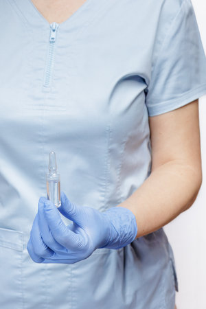 Female doctor in a blue glove holding an ampoule with medicine. Selective focus on the ampoule.の写真素材