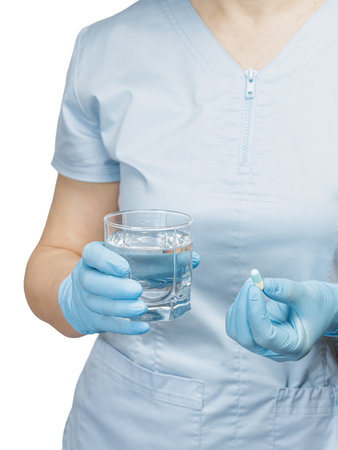 Close-up hands of a female physician with a glass of water in one hand and a capsule with medicine in another.の写真素材