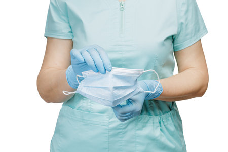 Hands of a female doctor in latex gloves holding the ready to use medical mask on the white background. Selective focus on the mask.の写真素材