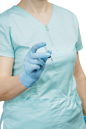 Female physician in a medical uniform and latex gloves holding a plastic syringe with medicine for injection on the white background. Selective focus on the syringe.の写真素材