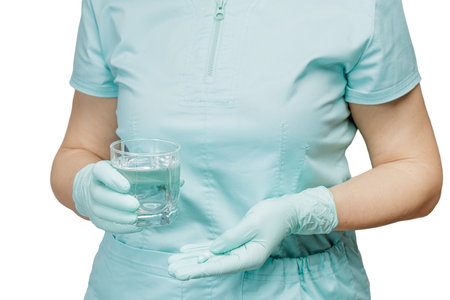 Close-up hands of a female physician with a glass of water in one hand and a capsule in another on the white background.の写真素材