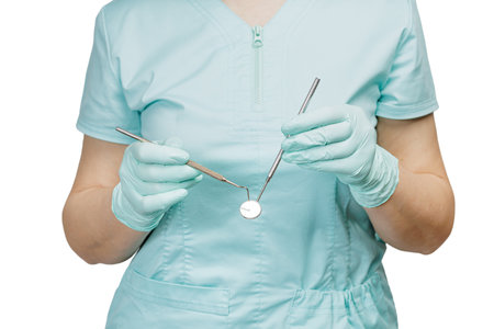 Dentist's hands in latex gloves with a probe and a metal mouth mirror on the white background. Medical tools concept.の写真素材