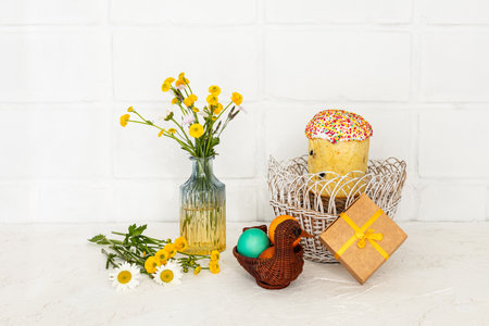 Easter cake and colored Easter eggs in the wicker baskets with a gift box. Yellow Ranunculus asiaticus in the glass vase.の写真素材