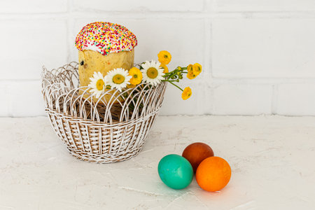 Easter cake with yellow Ranunculus asiaticus in the wicker basket. Colorful Easter eggs with a white wall on the background. Traditional Easter food.の写真素材