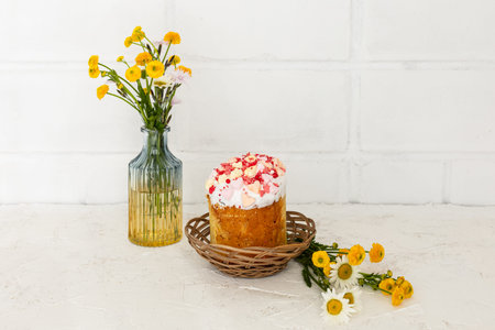 Easter cake in the wicker baskets with yellow Ranunculus asiaticus in the glass vase. White wall on...