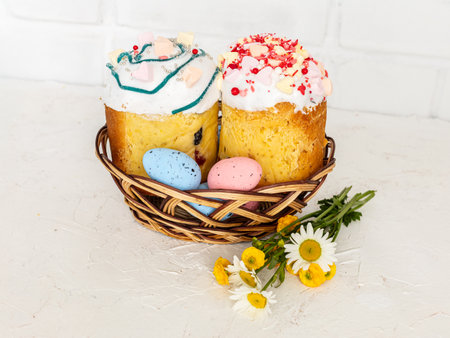 Sweet Easter cakes and colorful Easter eggs in the wicker basket with a white wall on the background.の写真素材