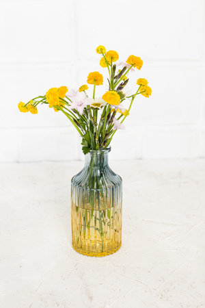 Bouquet of yellow flowers in the glass vase with a white wall on the backgroundの写真素材