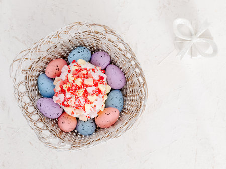 Sweet Easter cake and colorful Easter eggs in the wicker basket with a gift box on the white background. Top view.の写真素材