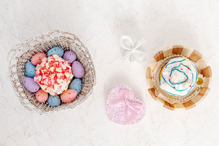 Sweet Easter cakes and colorful Easter eggs in the wooden baskets with gift boxes on the white background. Top view.の写真素材