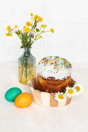 Easter cake, colorful Easter eggs and yellow Ranunculus asiaticus in the glass vase with a white...