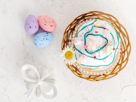 Sweet Easter cake in the wicker basket and colorful Easter eggs with a gift box on the white background. Top view.の写真素材