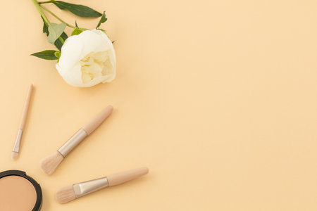Box with powder, brushes and a peony flower on the beige background. Women cosmetics. Top view.の写真素材