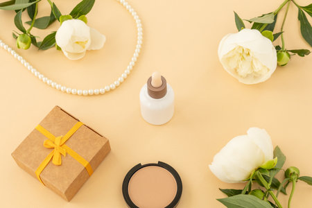 Facial serum, a gift box, powder and beads on the beige background. Women cosmetics and accessories. Top view.の写真素材