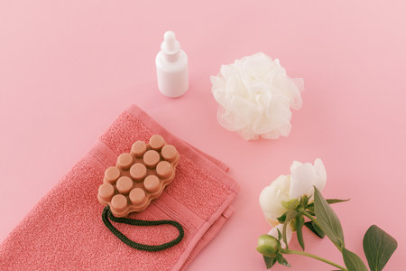Products for facial and body care. Soft terry towel with a soap, a facial serum, a sponge and a peony flower on the pink background. Spa and body care set. Top view.の写真素材