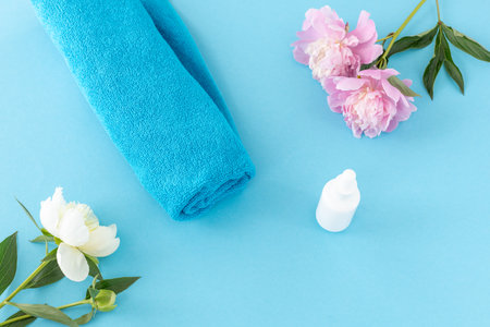 Products for facial and body care. Soft terry towel with a facial serum and peony flowers on the blue background. Spa and body care concept. Top view.の写真素材