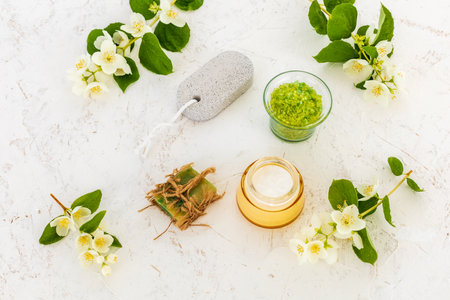 Products for facial and body care. Face cream, a bowl with sea salt, a soap, a pumice stone for feet and branches of jasmine on the white background. Spa and body care set. Top view.の写真素材