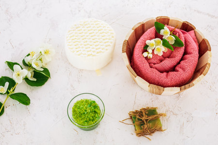 Products for facial and body care. Wooden basket with a soft terry towel, soap, a sponge, a bowl with sea salt and branches of jasmine on the white background. Spa and body care concept. Top view.の写真素材