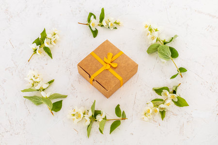 Gift box and branches of beautiful jasmine flowers on the white background. Top view. Concept of giving a gift on holidays.の写真素材