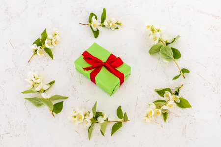 Green gift box and branches of beautiful jasmine flowers on the white background. Top view. Concept of giving a gift on holidays.の写真素材