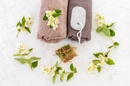 Products for facial and body care. Soft terry towels, a pumice stone for feet, a soap and branches of jasmine on the white background. Spa and body care set. Top view.の写真素材