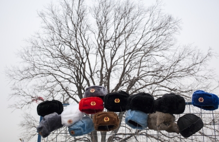 Russian military style fur hats displayed on a metal net at a street marketの写真素材