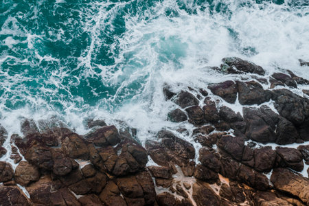 Aerial view of crashing waves on rocks. Background texture of a rocky shore and blue and turquoise...