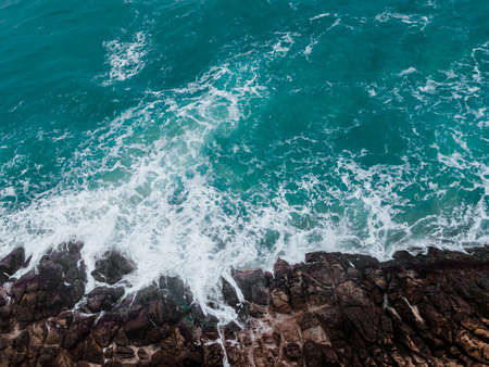Aerial view of crashing waves on rocks. Background texture of a rocky shore and blue and turquoise seaの写真素材