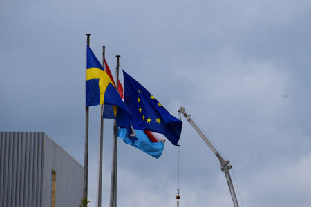 Swedish, Luxembourgish and European Union flags waving in the wind on a cloudy day