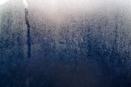 small droplets of water on dark blue glass, behind the glass is lit by the light of a lanternの写真素材
