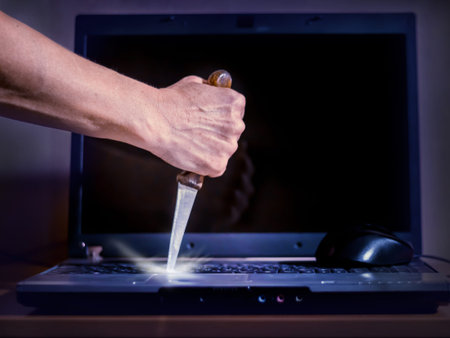 hand with a knife in the laptop keyboard, a symbol of irritation and anger due to prolonged work at...
