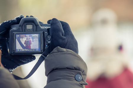 hands in mittens holding a professional camera, the screen image of posing models, winter dayのeditorial素材